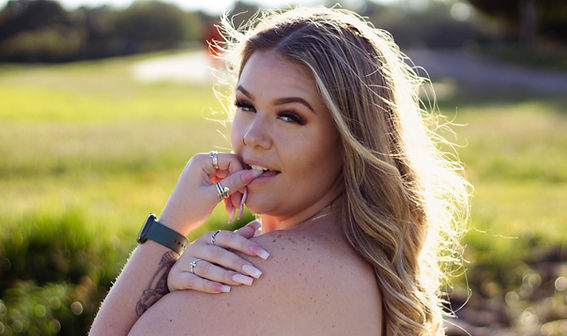 Woman posing outdoors in a grassy field during a soft natural-light portrait session.