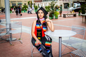 Graduate wearing a cap, gown, and stole while standing outdoors on campus.