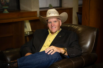 Man wearing a cowboy hat seated in a leather chair for a portrait.