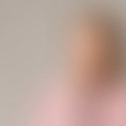 A woman in a pink sweater smiles subtly, touching her chin, against a plain beige background. She wears red earrings. The mood is thoughtful.