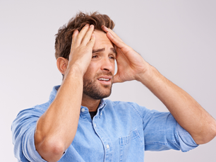 Man in a blue denim shirt holds his head with both hands, expressing stress or worry. Gray background enhances the tense mood.