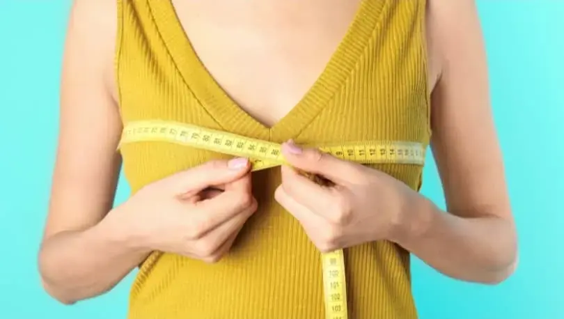 A woman measuring her bust size with a measuring tape