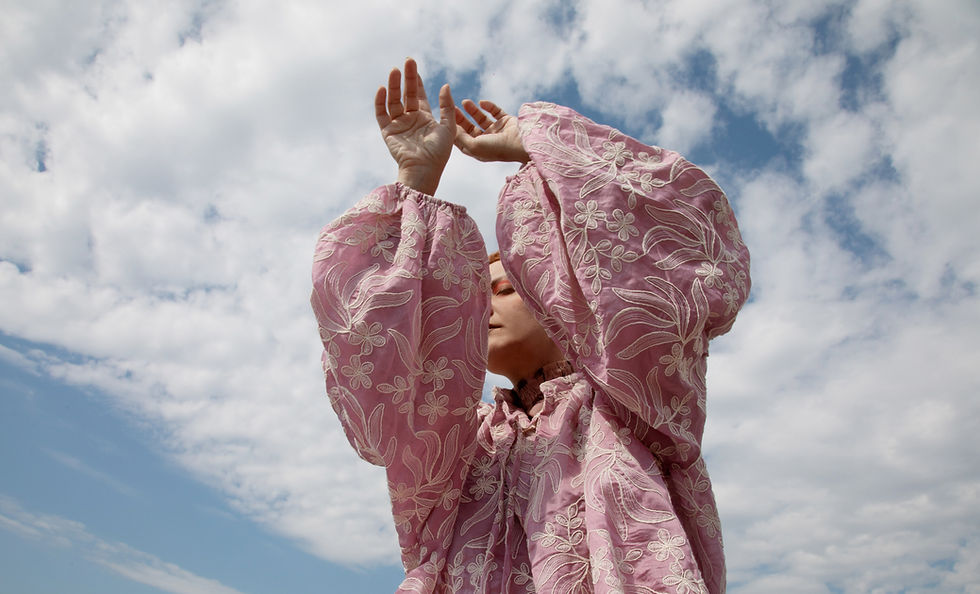 Woman in pink floral blouse raising hands against blue sky