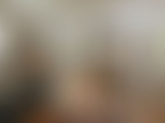 Cozy kitchen with dark cabinets, wood countertops, central island with a plant and candle. Hanging utensils, spices, and cutting boards adorn walls.