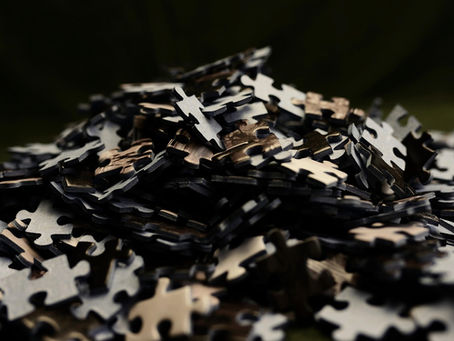 A pile of black and beige puzzle pieces on a dark surface, creating a textured, mysterious atmosphere. No text visible.