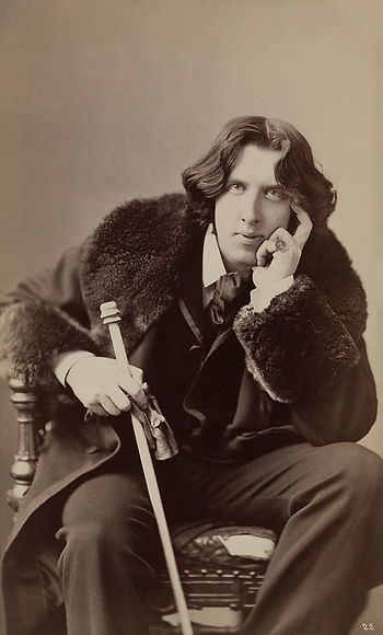 A photograph of a young Oscar Wilde, sitting in a chair with a cane.