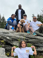 Five people and a dog on a rocky mountain, girl flexing arms