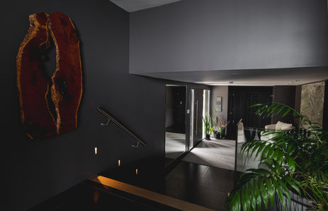 Dark entry and stairway with a live-edge wood wall sculpture, step lights and a glass railing