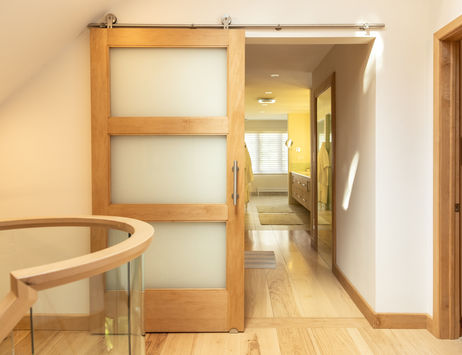 Wood sliding barn door with frosted glass panels beside a curved glass stair railing