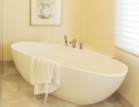 Freestanding soaker tub tucked into a corner of a bright ensuite with a framed floral print
