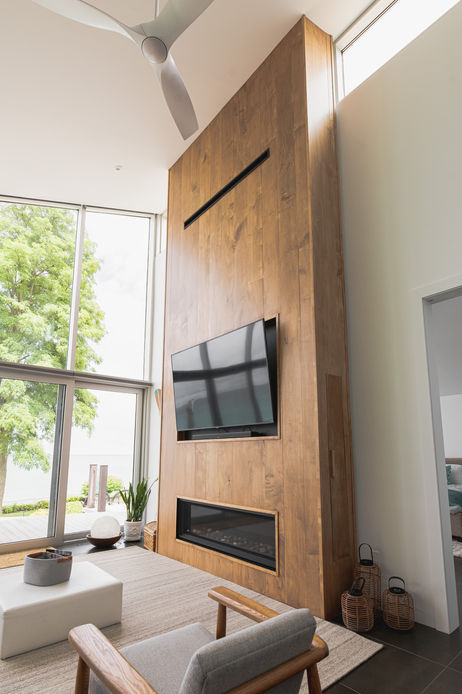 Two-storey wood fireplace wall with a linear gas fireplace and recessed TV beside tall windows