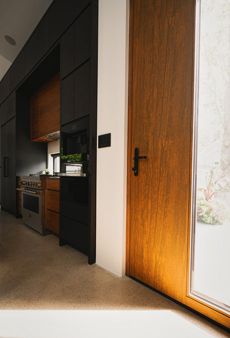 Tall wood-grain door beside black kitchen cabinets, a gas range and polished concrete floors