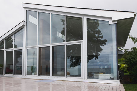 Close-up of a white-framed glass curtain wall and sliding doors reflecting trees and sky
