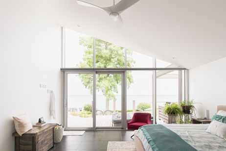 Main bedroom with a sloped ceiling and glass wall with sliding doors opening to the deck and lake