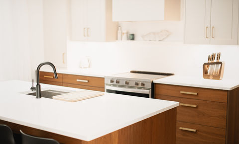 White quartz kitchen island with a workstation sink beside walnut lower cabinets with brass pulls
