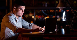 man working on a laptop at night building a side hustle while working full-time