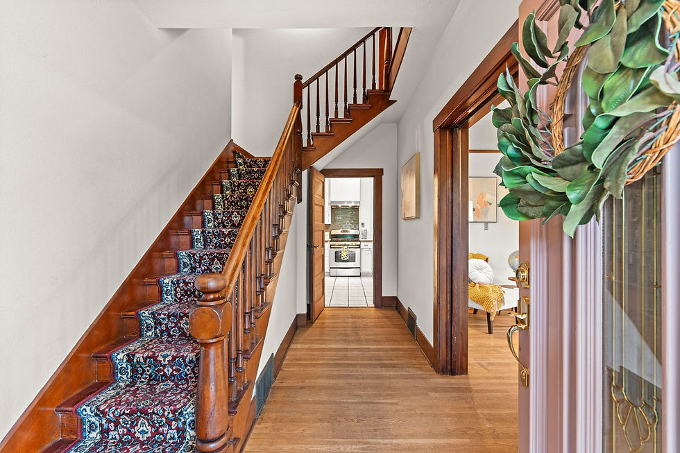 Wooden staircase with patterned runner in a bright hallway, open door to kitchen, wreath on glass door, cozy home interior