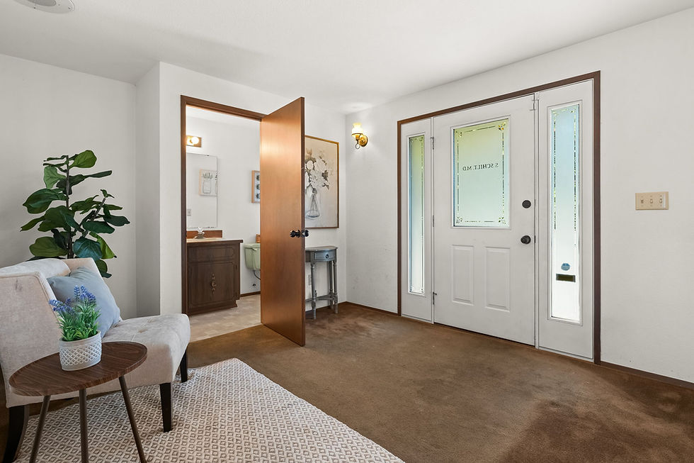 Bright waiting room entry with open wooden door, white front door, beige chair, plant, and small table.