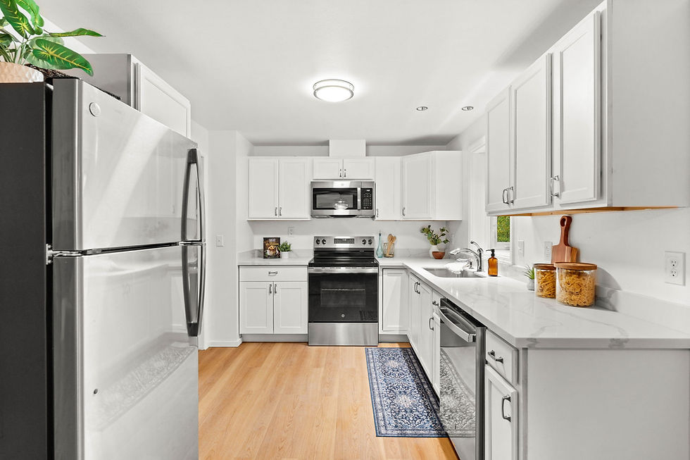 Modern kitchen with white cabinets, stainless steel appliances, and wooden floor. Green plant on fridge, glass jars on counter, cozy vibe.