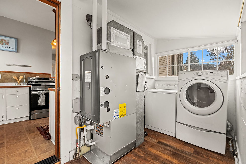 Laundry and utility room with a white washer and dryer, gray furnace, wood flooring, and view of blue sky through a window. Kitchen visible.