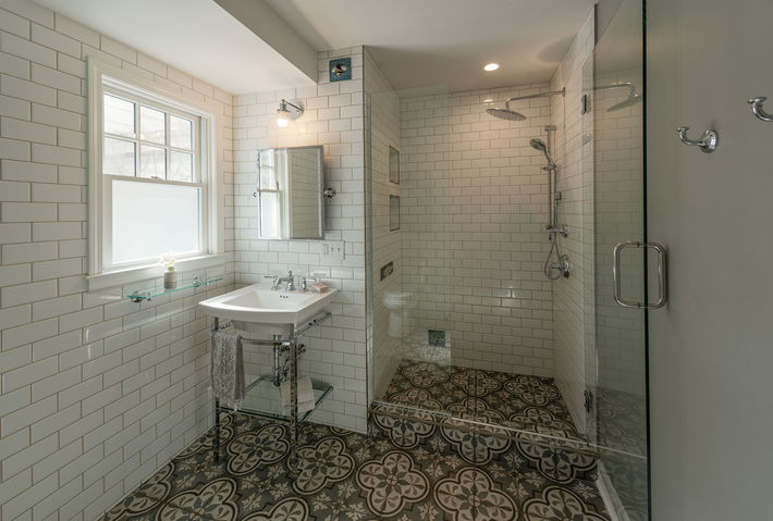Fully subway-tiled bathroom with walk-in shower, decorative ceramic floor tile and console sink