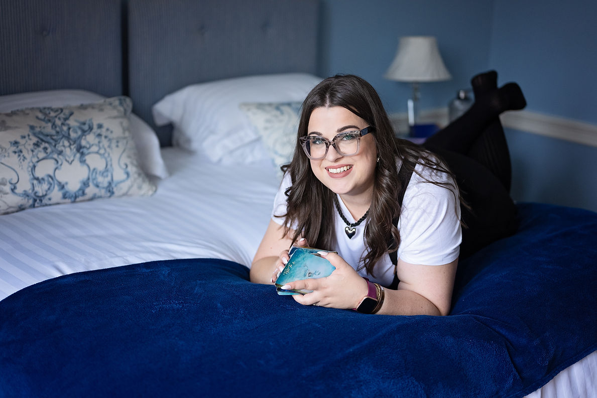 woman-with-dark-hair-wearing-glasses-resting-on-bed-in-blue-room-with-deck-of-tarot-cards-