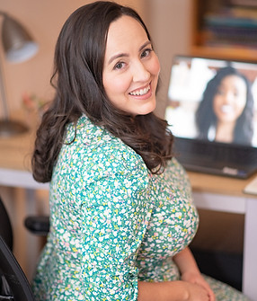 brunette-woman-in-green-dress-sitting-at-table-working-on-laptop-turned-dacing -the-person