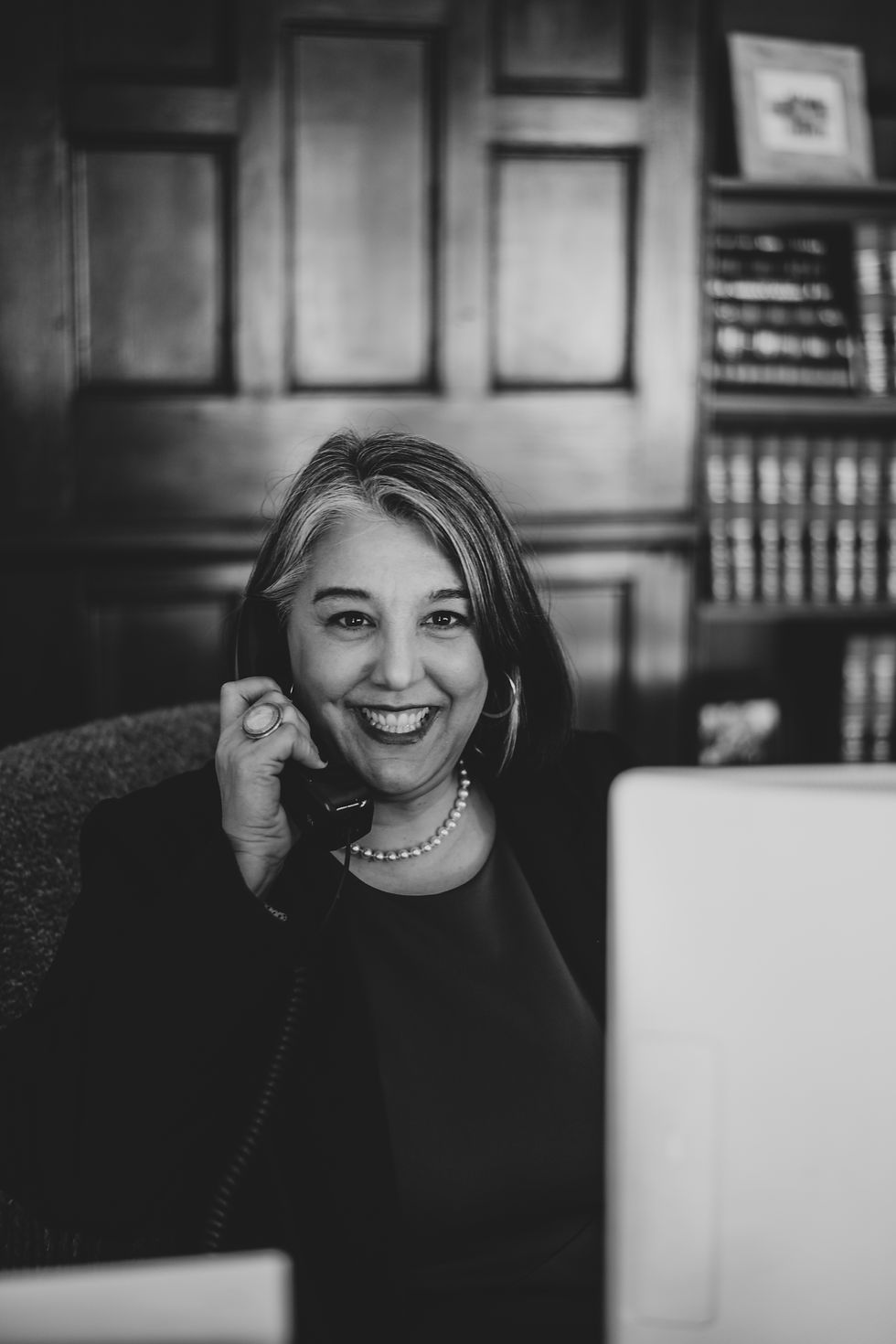Smiling woman on the phone in an office with wooden panels and bookshelves in the background. Black and white image.