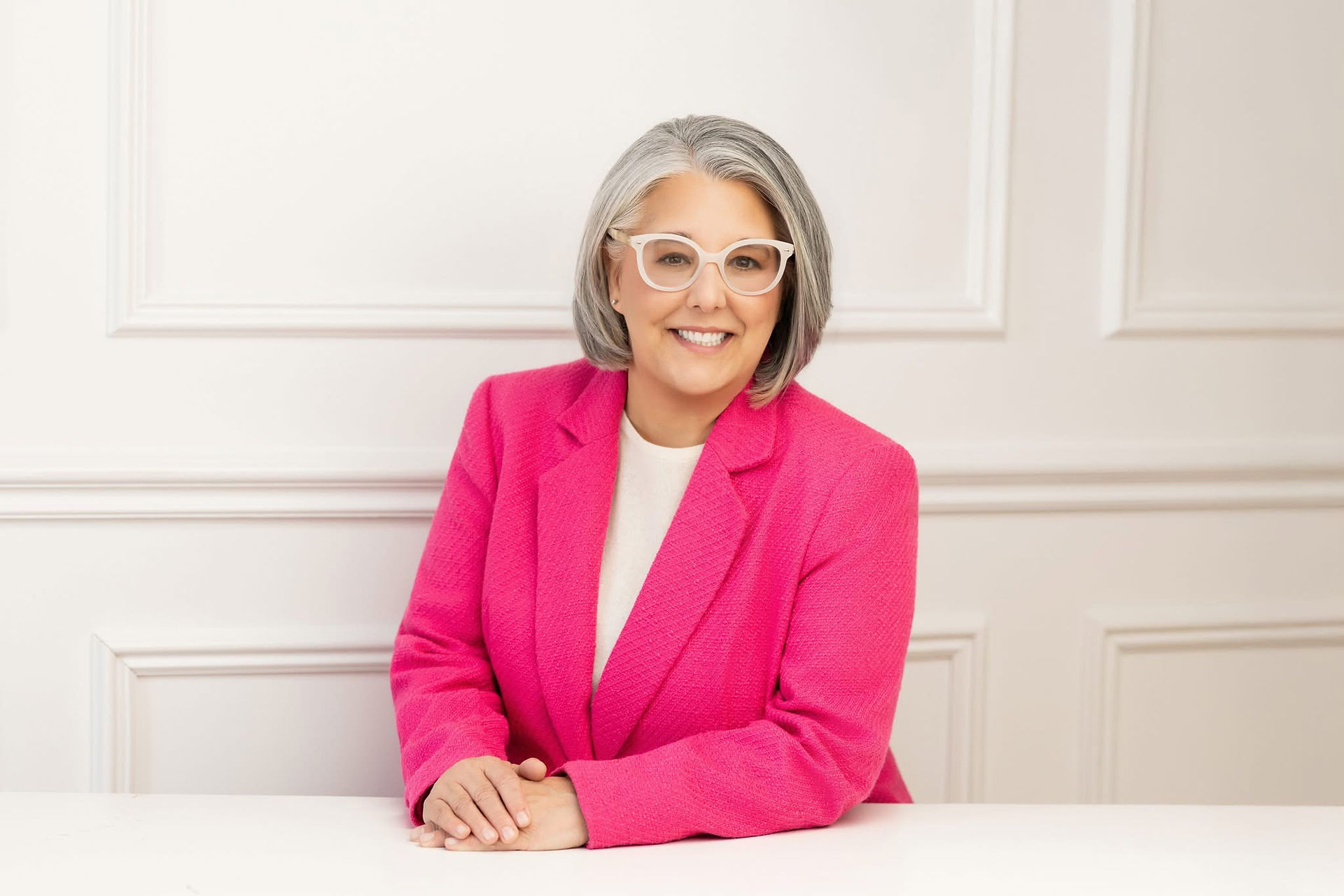 Woman in pink jacket, wearing glasses, smiling