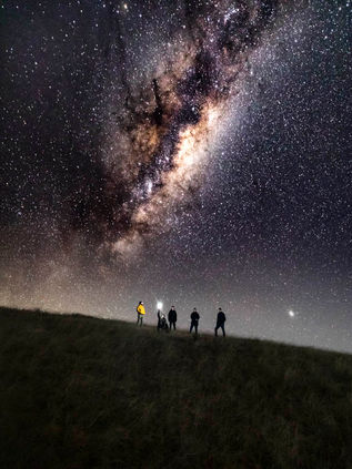 Silhouettes of people on a hill under the Milky Way galaxy.