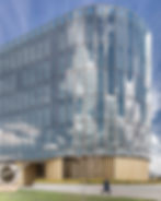 Curved glass building facade reflecting the sky, with a pedestrian at street level.