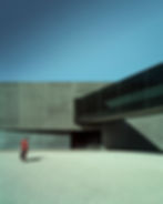 Minimalist architectural composition with strong shadows, blue sky and a lone person in a concrete courtyard.