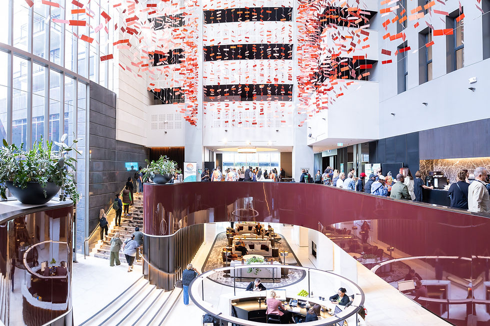 Event guests in a light-filled Canberra atrium beneath a suspended art installation, photographed by Ari Rex