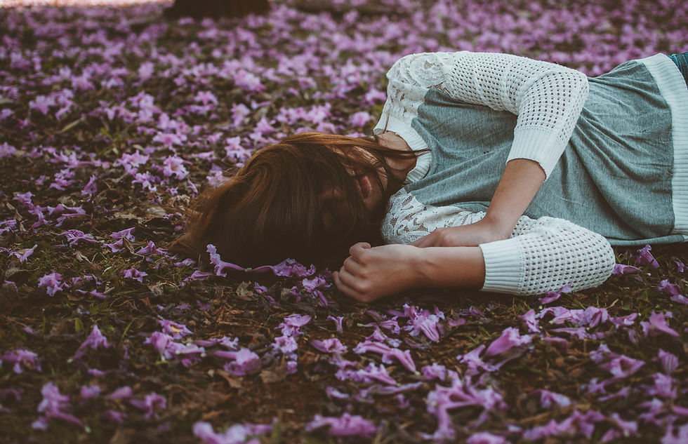 A woman in a lace-sleeved sweater quietly rests on a blanket of purple blossoms, blending with the serene beauty of nature.