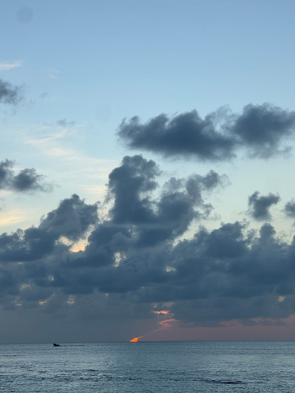 A sliver of orange sunset slips between dark clouds over a deep blue ocean.