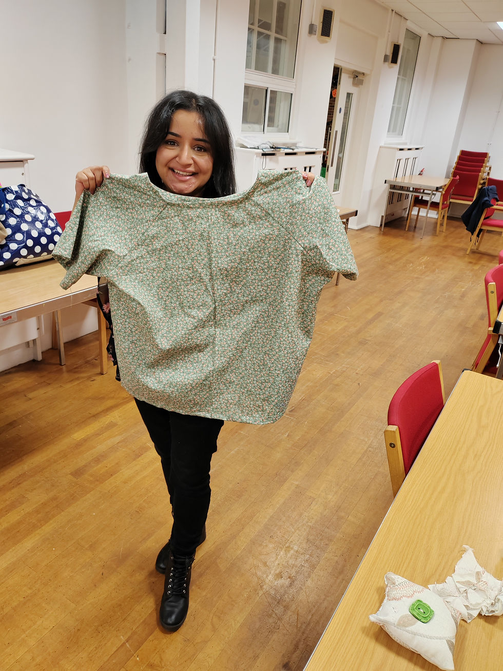 Smiling woman holds up sewn top from local sewing classes.