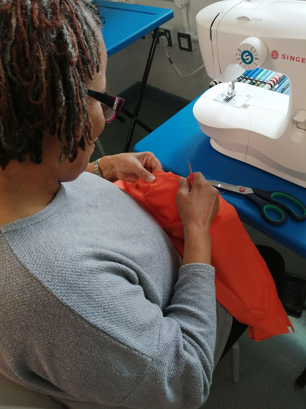 Woman sewing orange fabric on a machine for local sewing classes.