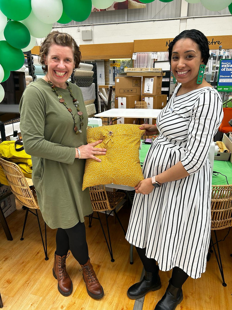 Two smiling women holding a yellow decorative pillow