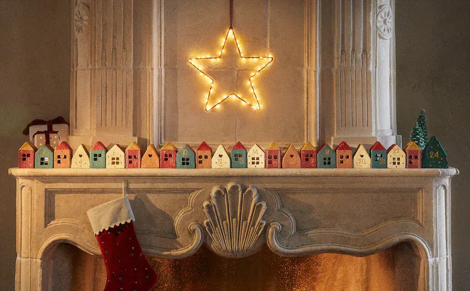 La estrella iluminada hace que la decoración de esta chimenéa de piedra brille todavía más. Candelabros con forma de casitas de ceráica en colores rojo, naranja, azul y blanco. Todo de Zara Home.