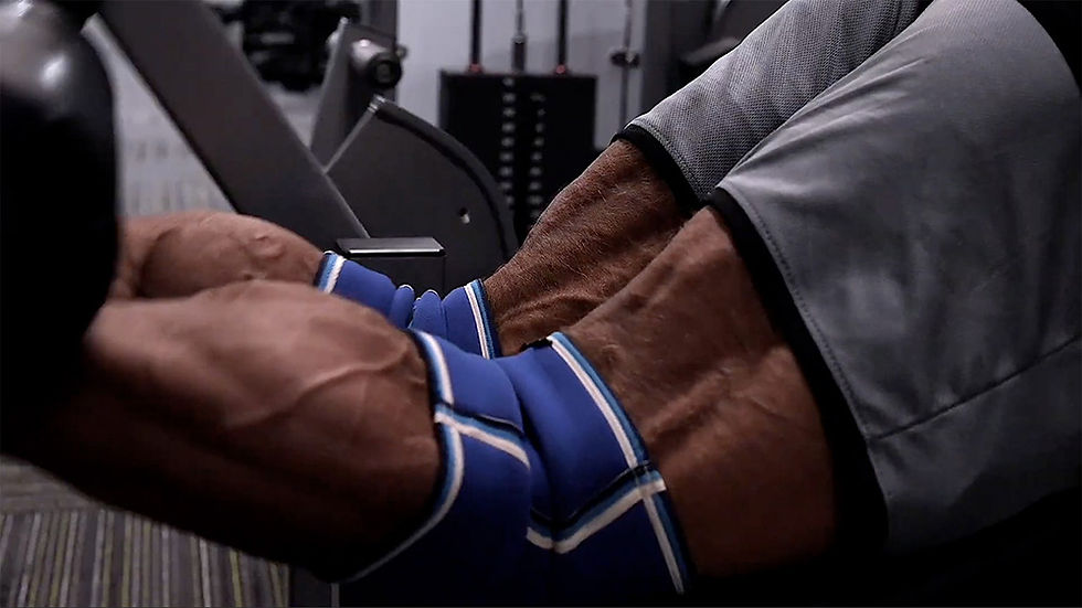 Muscular legs perform leg curl on gym machine, legs wrapped in blue sleeves. The setting is a gym with a focused, intense mood.