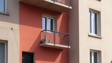 Façade d'immeuble beige et rouge avec balcons en métal noir. Porte noire en bas. Fenêtres rectangulaires. Ambiance tranquille. Immeuble sans syndic de copropriété