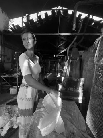 Giulia Mastrangelo is at the glass foundry, carefully working on her latest glass piece. She glances forward with a smile on her face, reflecting her joy and connection to the artistic process.