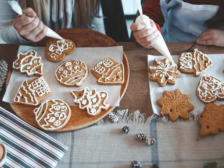 Kaksi lasta koristelee joulupipareita kuorrutteella puualustalla. Taustalla näkyy käpyjä ja raidallinen liina. Iloinen tunnelma.