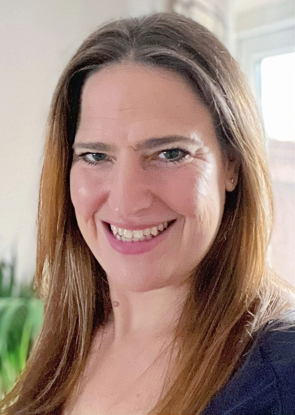 Headshot of Catherine: the founder of English Home Studies. Smiling woman with long brown hair in a bright room and wearing a black top.