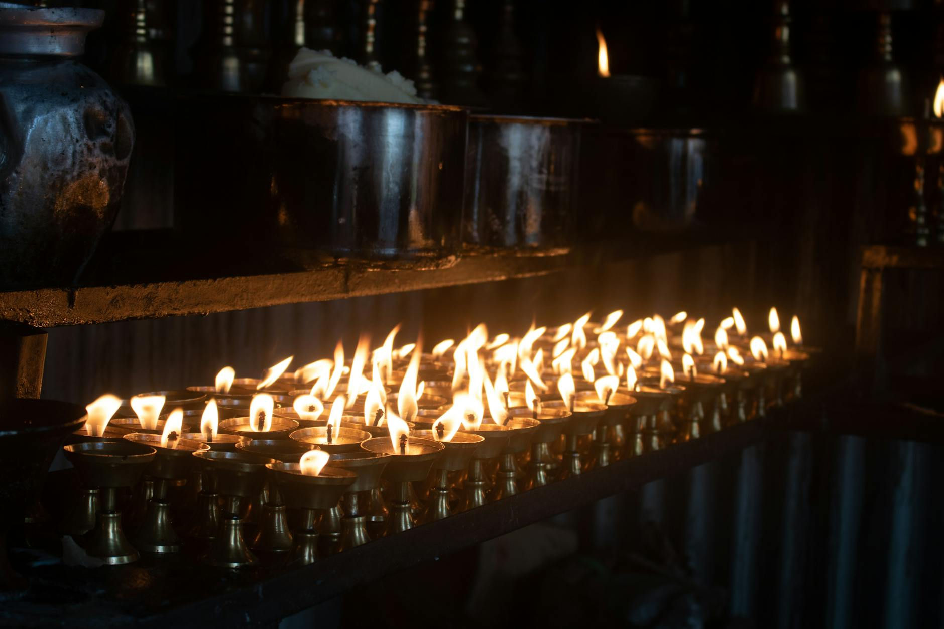 Rows of small glowing oil lamps in a dark room