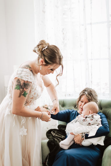 Woman fixes baby's bracelet, a mother holds the baby on a green couch, indoors.