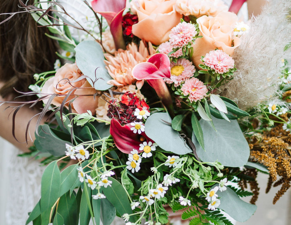 Woman holding colorful wedding bouquet with roses, greenery, and various flowers.