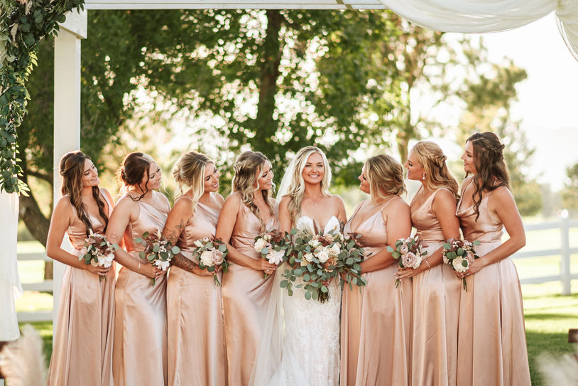 Bride smiles with bridesmaids in matching dresses about her at wedding ceremony