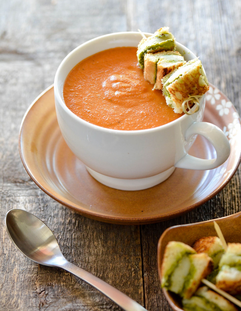 A cup of tomato bisque with grilled cheese and pesto croutons