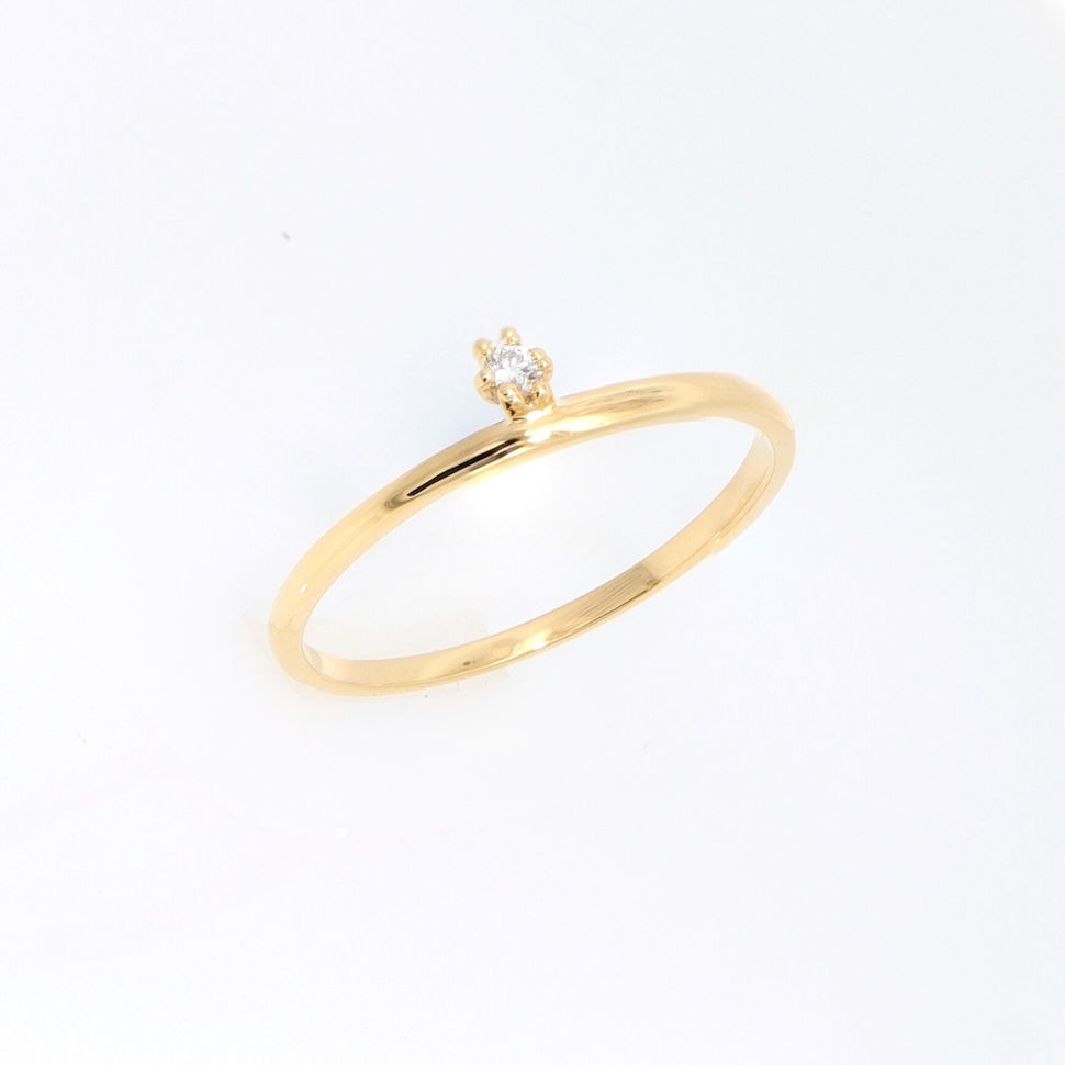Minimalist diamond ring with a single off-center round diamond on a thin fine gold band.